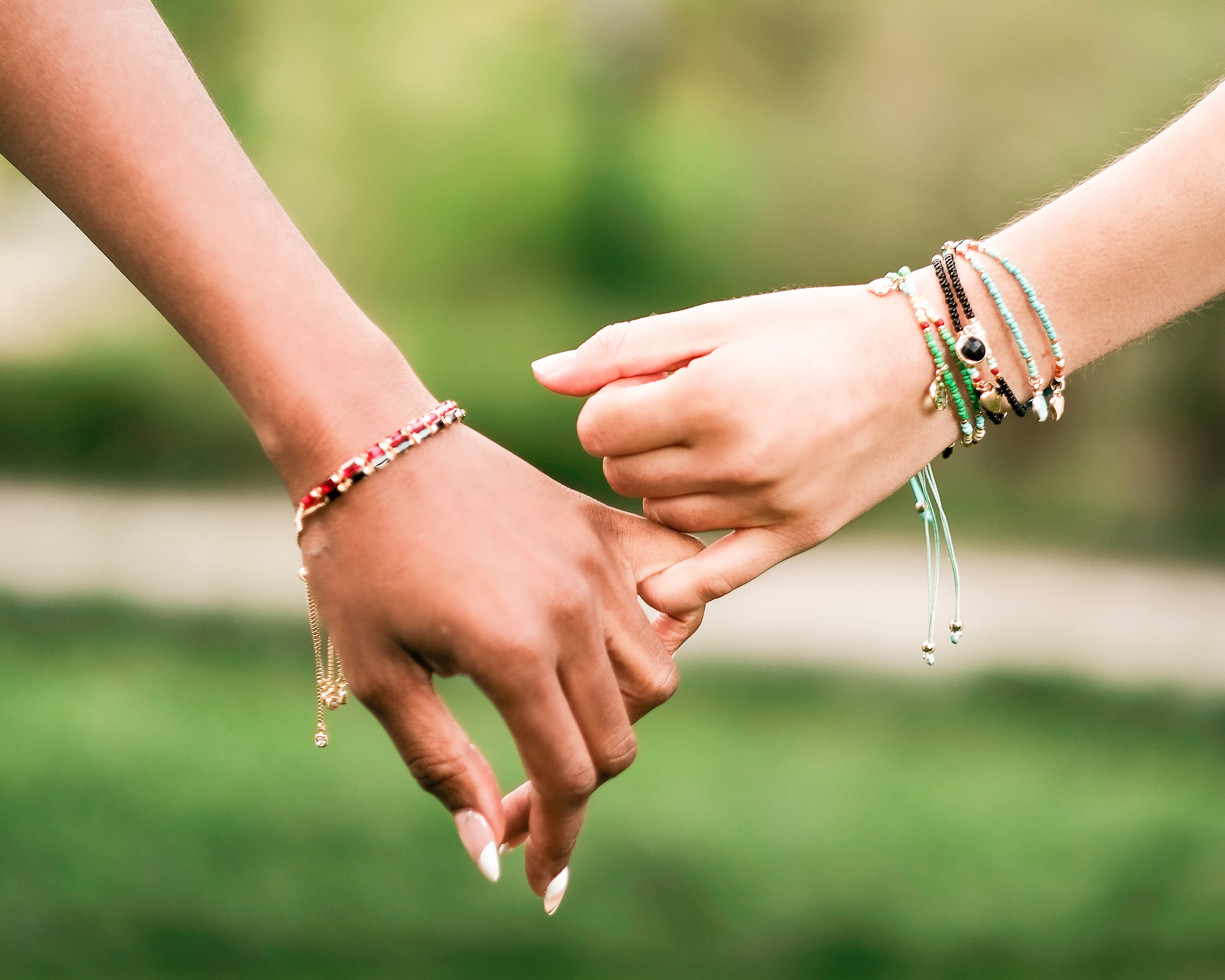 Close-up of two people holding hands, both wearing My Fancy Flamingo’s layered pearl and gold charm bracelets — perfect friendship jewelry.