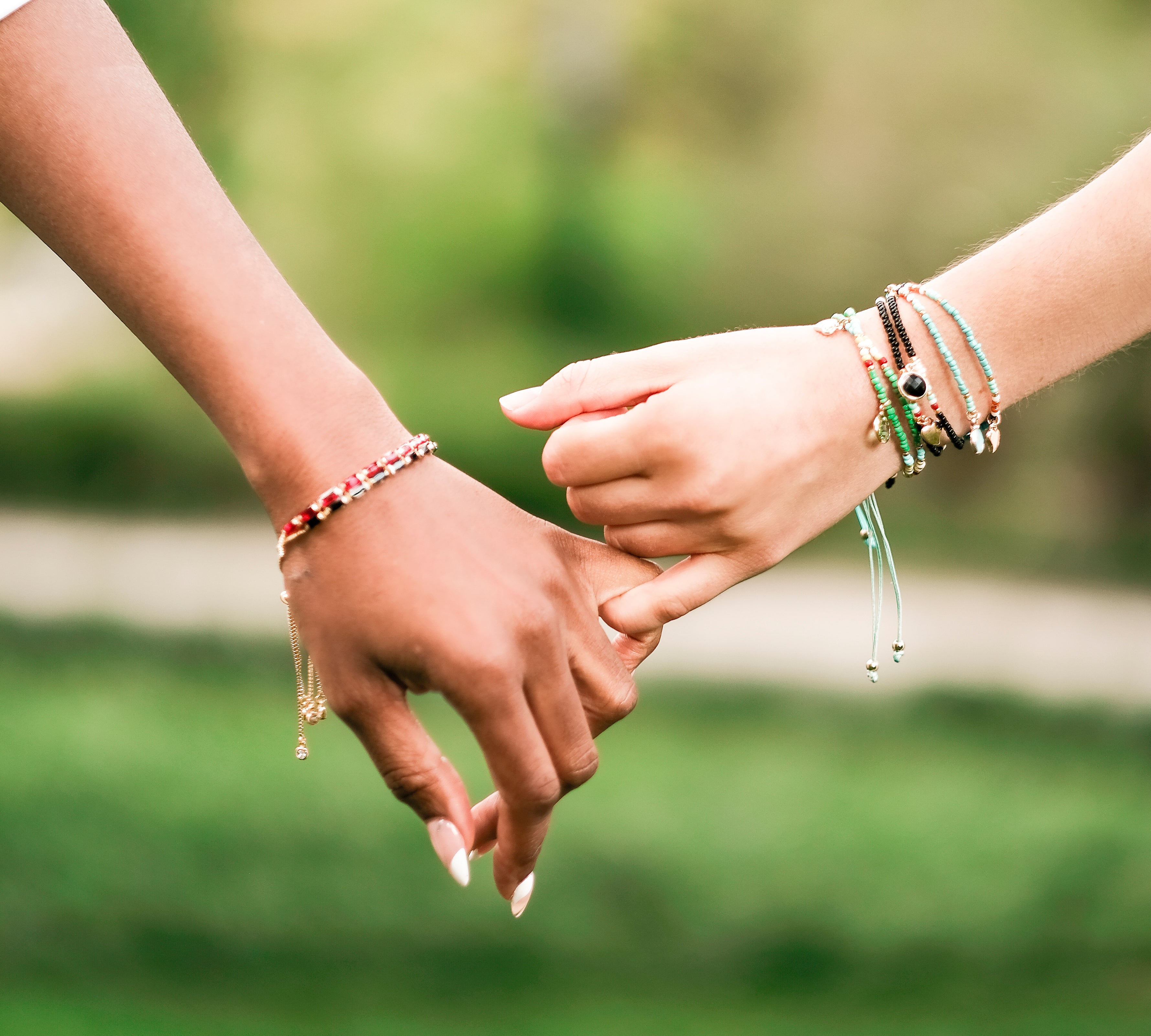 Close-up of two people holding hands, both wearing My Fancy Flamingo’s layered pearl and gold charm bracelets — perfect friendship jewelry.