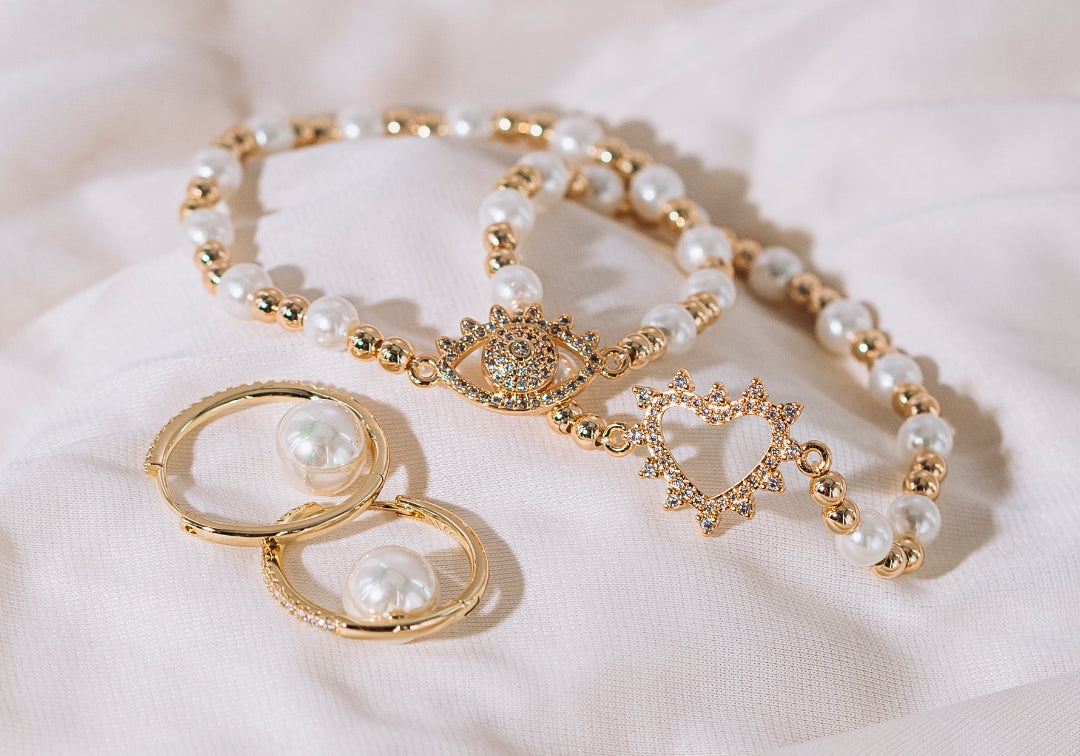 gold bracelet with pearls and evil eye on silk background with gold pearl hoop earrings