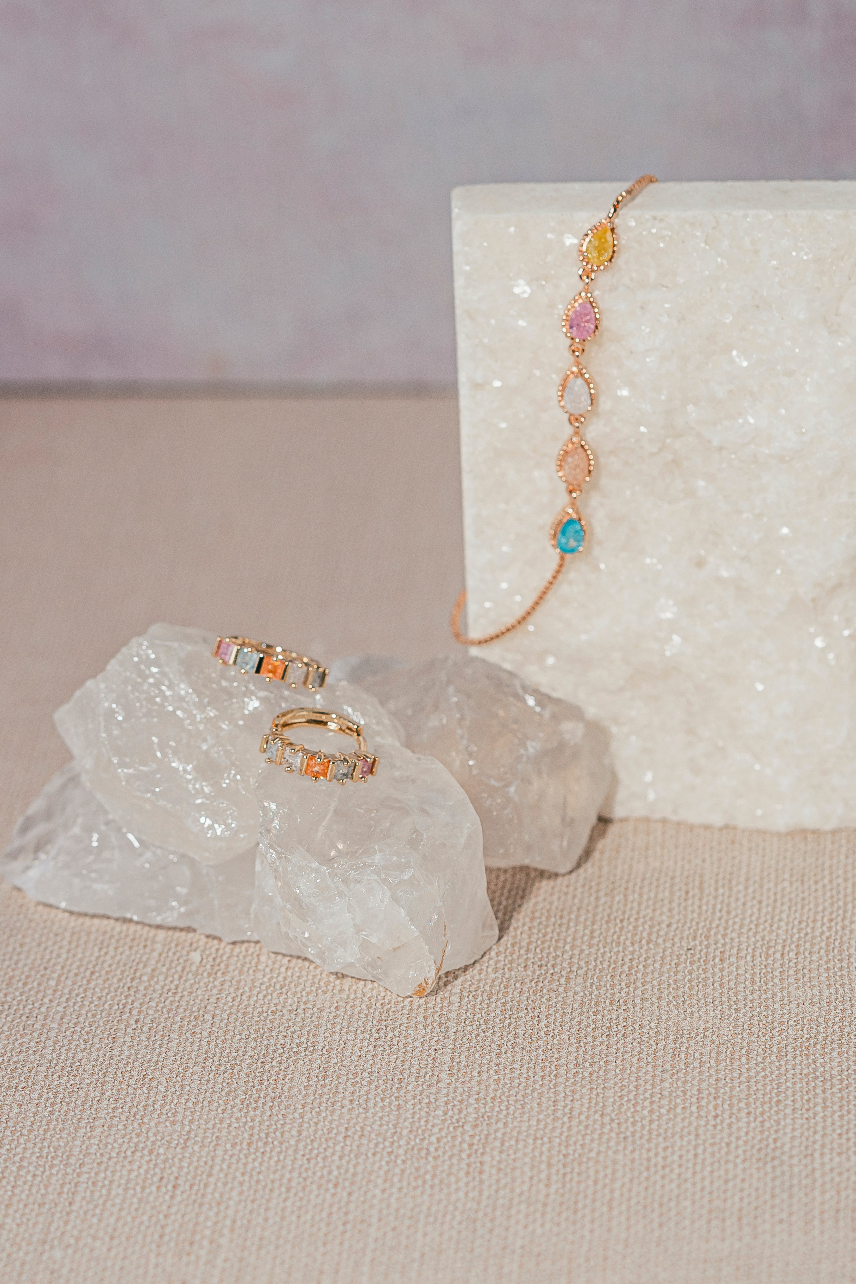 Colorful dainty bracelet with gemstone teardrops and matching rainbow baguette hoop earrings styled on crystals — vibrant summer jewelry collection from My Fancy Flamingo
